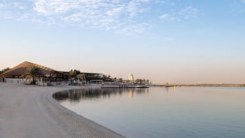 Ein Strand mit sandigem Ufer, ein Gebäude mit geneigtem Dach und ruhigem Gewässer, das den Himmel spiegelt.