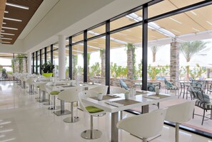 A modern indoor dining area with white tables and chairs, large windows, and a view of the outdoors. - Yas Plaza Bay (Abu Dhabi)