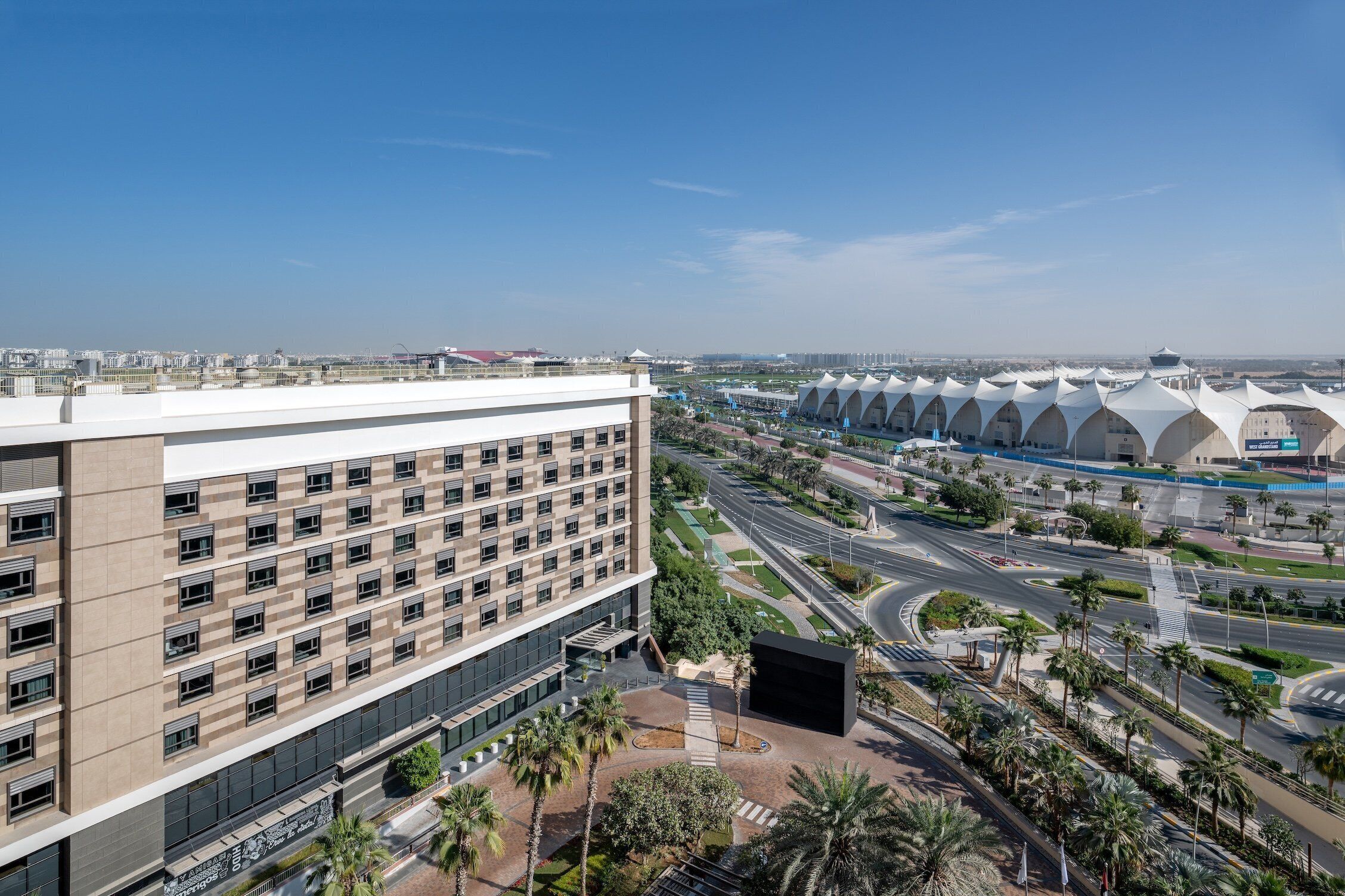 Un hotel moderno con varios pisos, un patio central y vistas a un paisaje urbano con arquitectura distintiva.