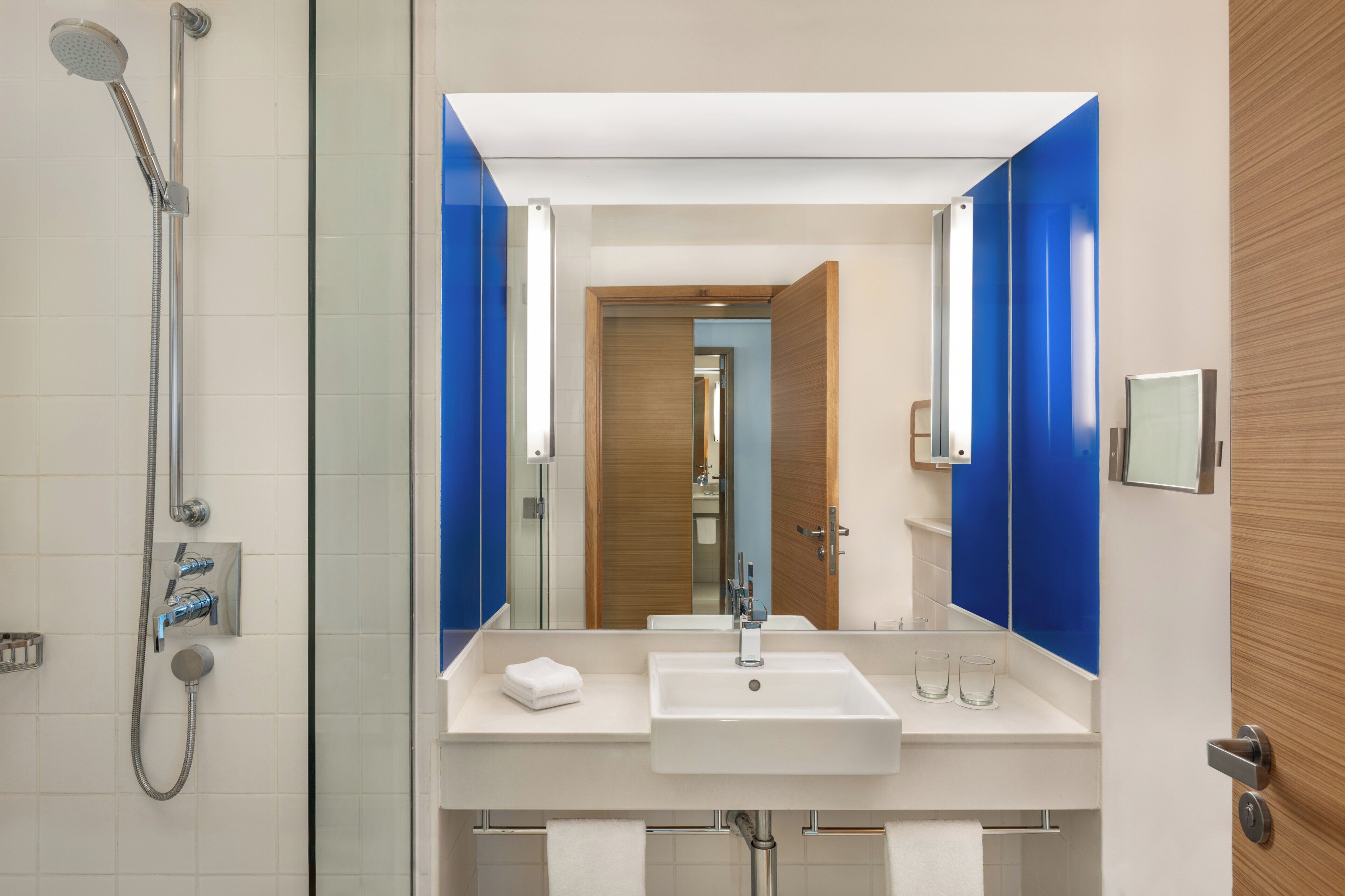 A modern bathroom with a glass-enclosed shower, a white sink, and a large mirror with blue accents.