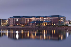 A multi-story hotel with a stone facade, large windows, and a reflection in the water in front. - Homewood Suites by Hilton Denton (Denton)