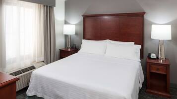 A hotel room with a large bed, two bedside tables with lamps, a heater, and a window with curtains.