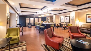 A hotel lobby with a central dining area, multiple seating options including chairs and sofas, and a reception desk.