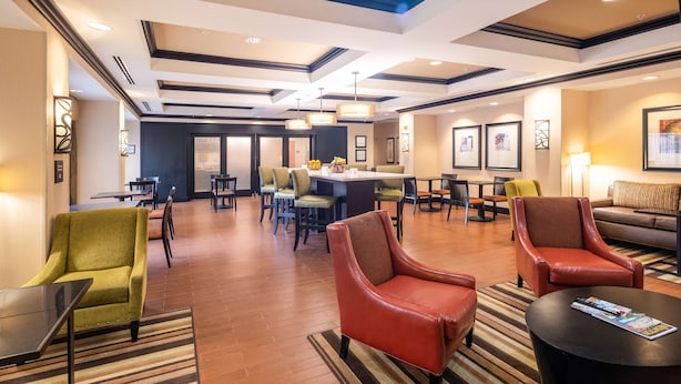Una hall d'albergo con un'area ristoro centrale, diverse opzioni di seduta tra cui sedie e divani, e una reception.