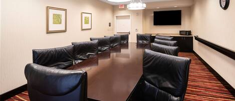A conference room with a long table, leather chairs, a clock on the wall, and a flat-screen TV.