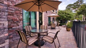 An outdoor patio with a brick wall, a round table with striped chairs, and two large umbrellas. - Hampton Inn & Suites Jacksonville - Beach Blvd/Mayo Clinic (Jacksonville)