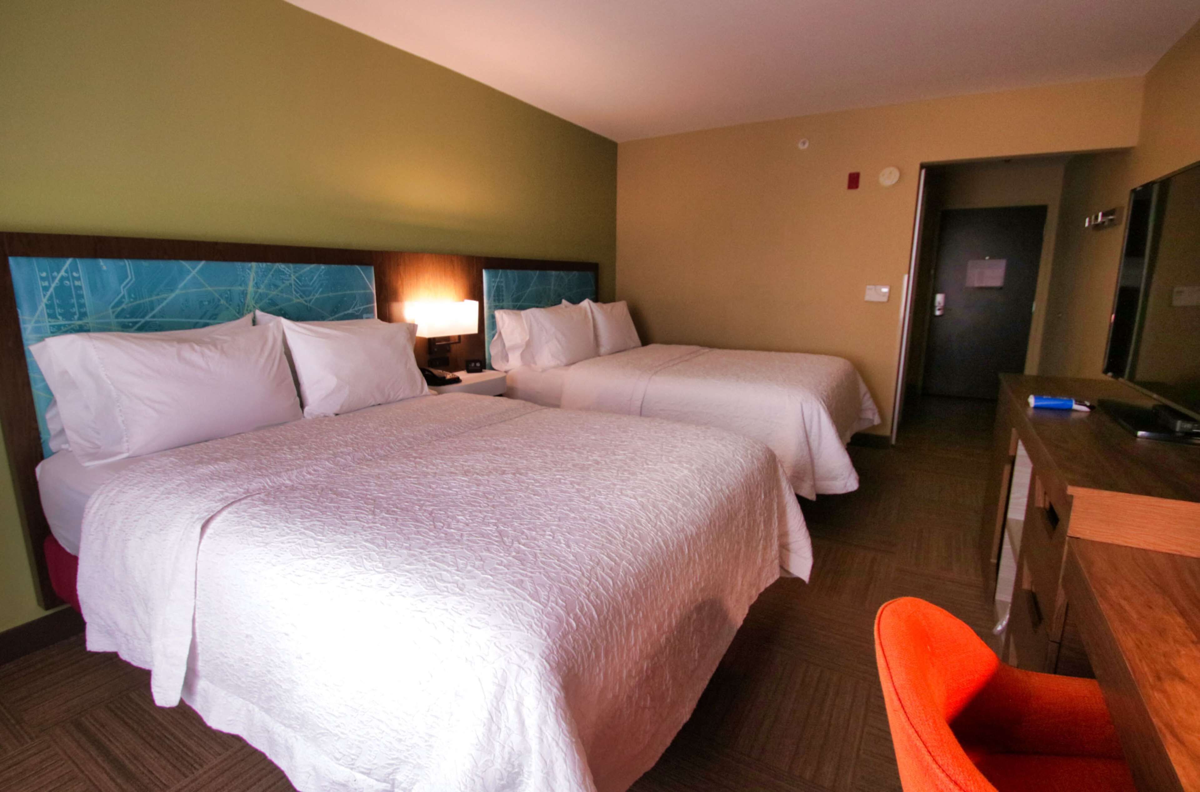 A hotel room with two beds, a desk, a chair, and a mirror.