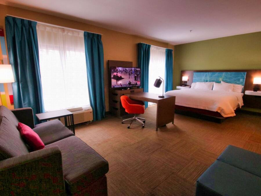 Una habitación de hotel con cama, escritorio, silla, televisor y sofá.