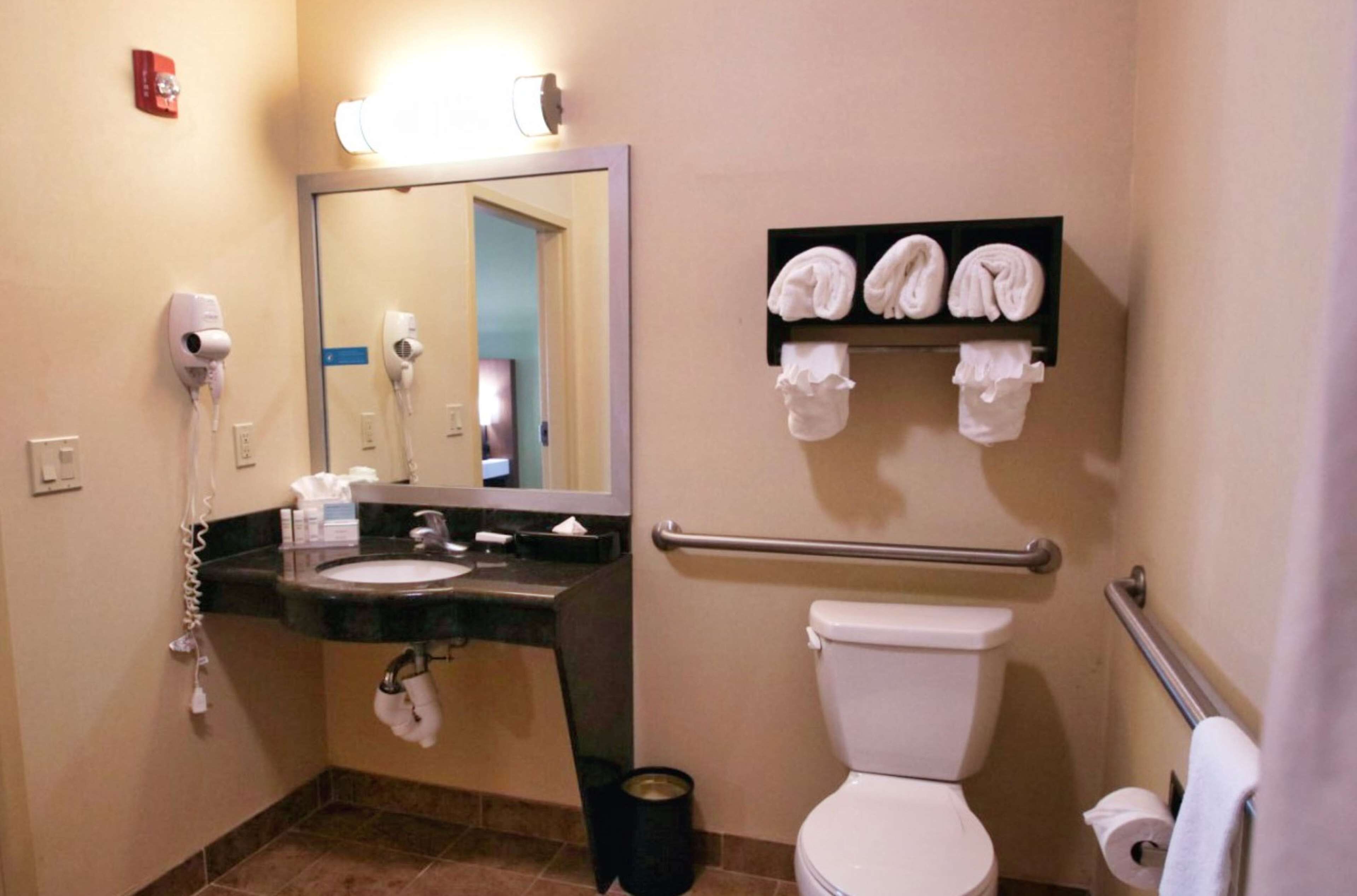 Un baño con lavamanos, espejo, toallero y retrete.