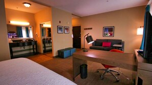 A hotel room with a bed, a desk, a sofa, and a small table. There is a mirror, a lamp, and a picture on the wall. - Hampton Inn & Suites Jacksonville - Beach Blvd/Mayo Clinic (Jacksonville)