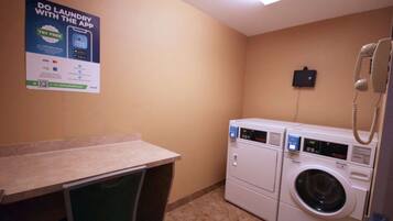 A laundry area with a poster advertising a laundry app, a washing machine, a dryer, a phone, and a small table.