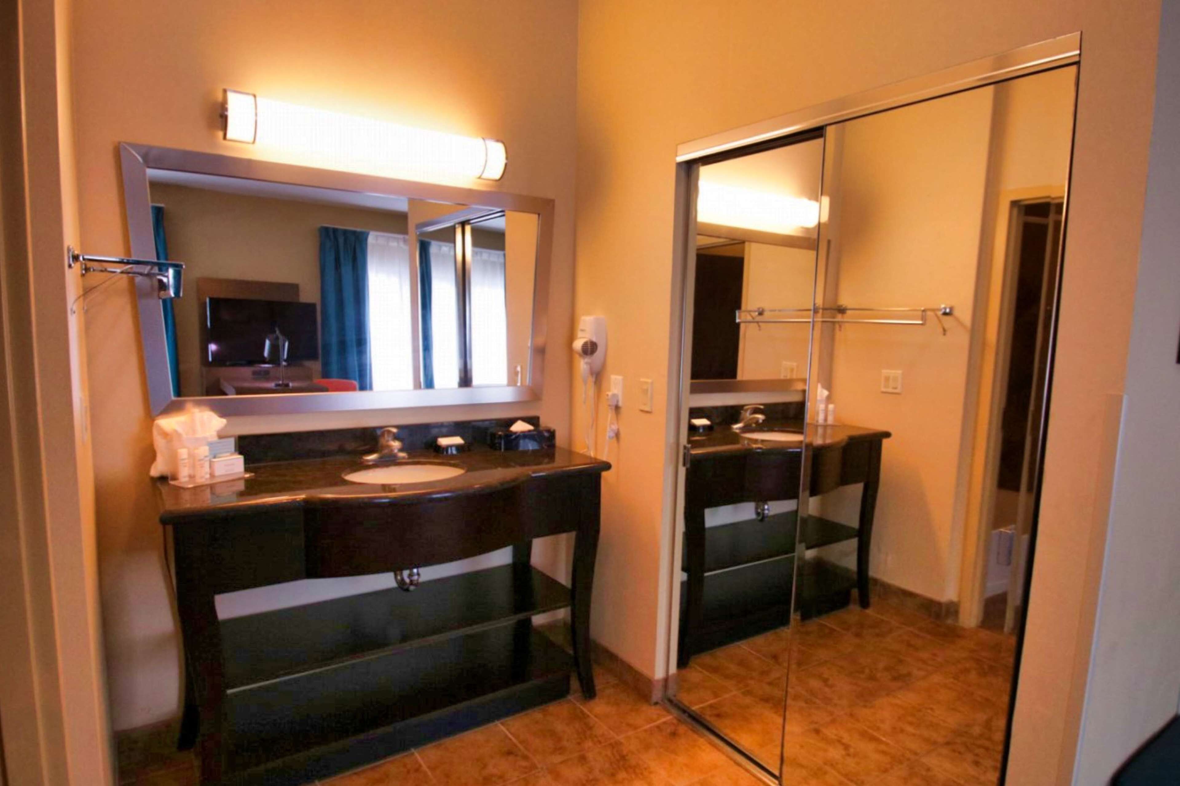 Ein Hotelbadezimmer mit einem dunklen Holz-Waschtisch, einem großen Spiegel und einer Duschkabine aus Glas.