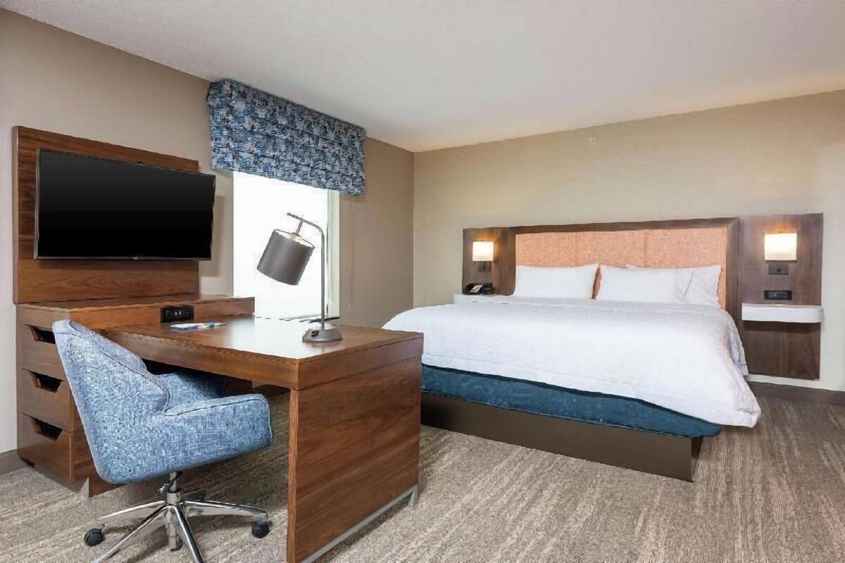 A hotel room with a bed, a desk with a chair, a television, and a lamp.
