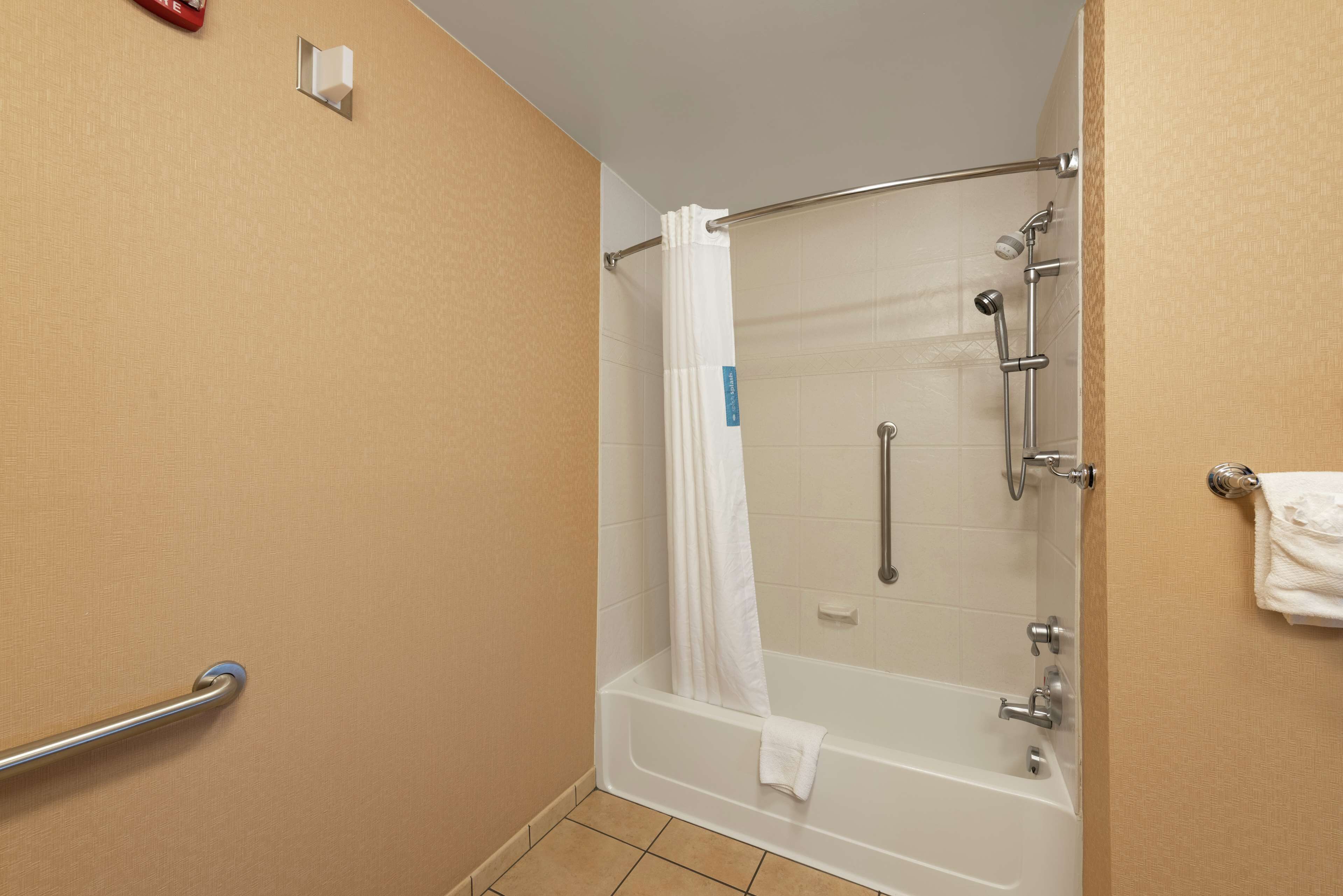 A shower area with a bathtub, a handrail, and a towel rack.