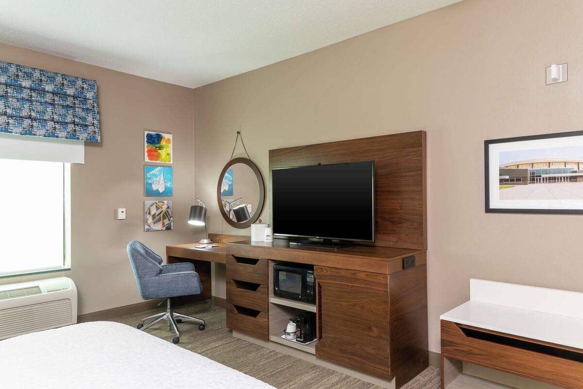 A hotel room with a bed, a desk with a computer, a TV, a microwave, and a coffee maker.