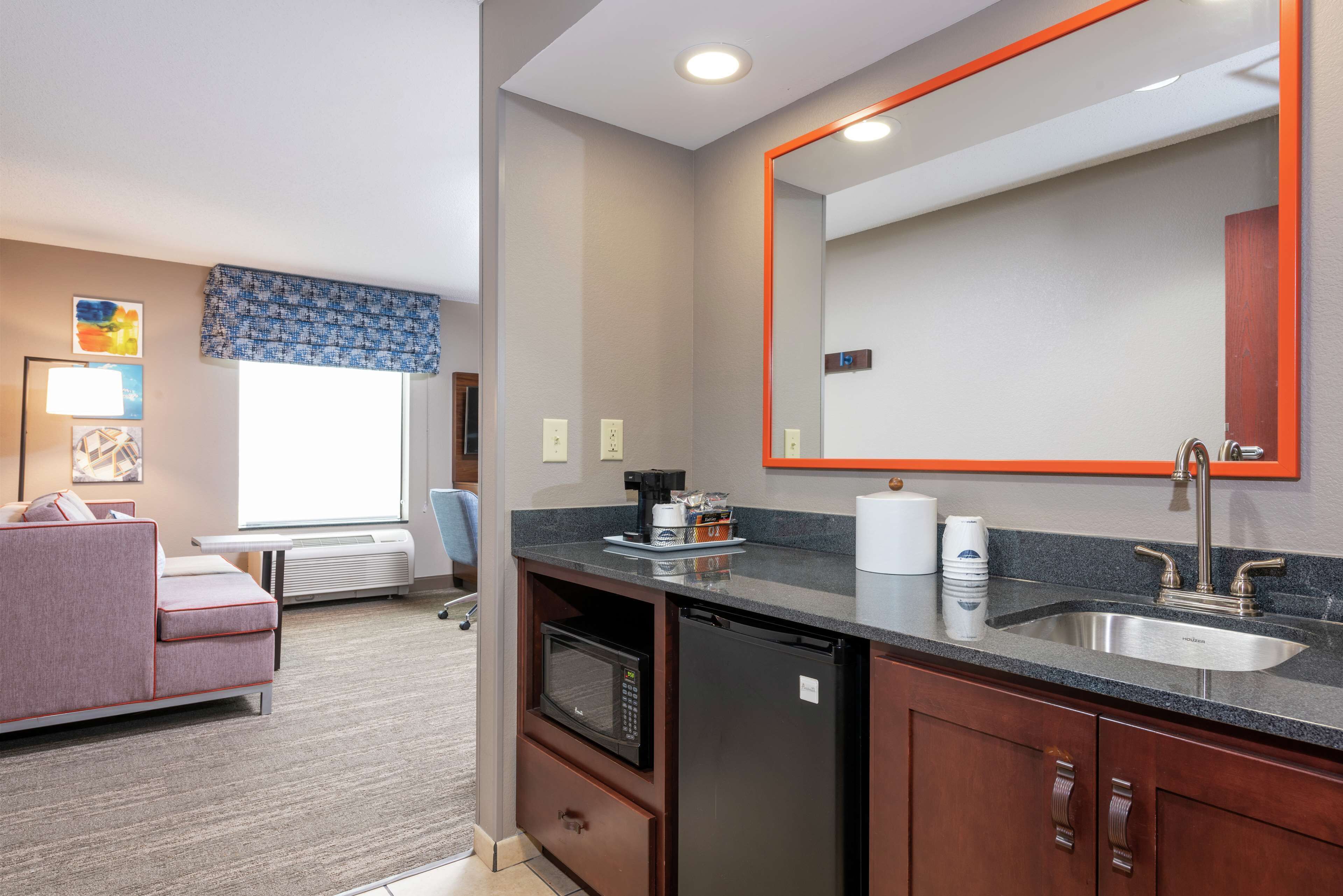 Habitación de hotel compacta con kitchenette, un espejo grande, sofá y ventana con vistas.