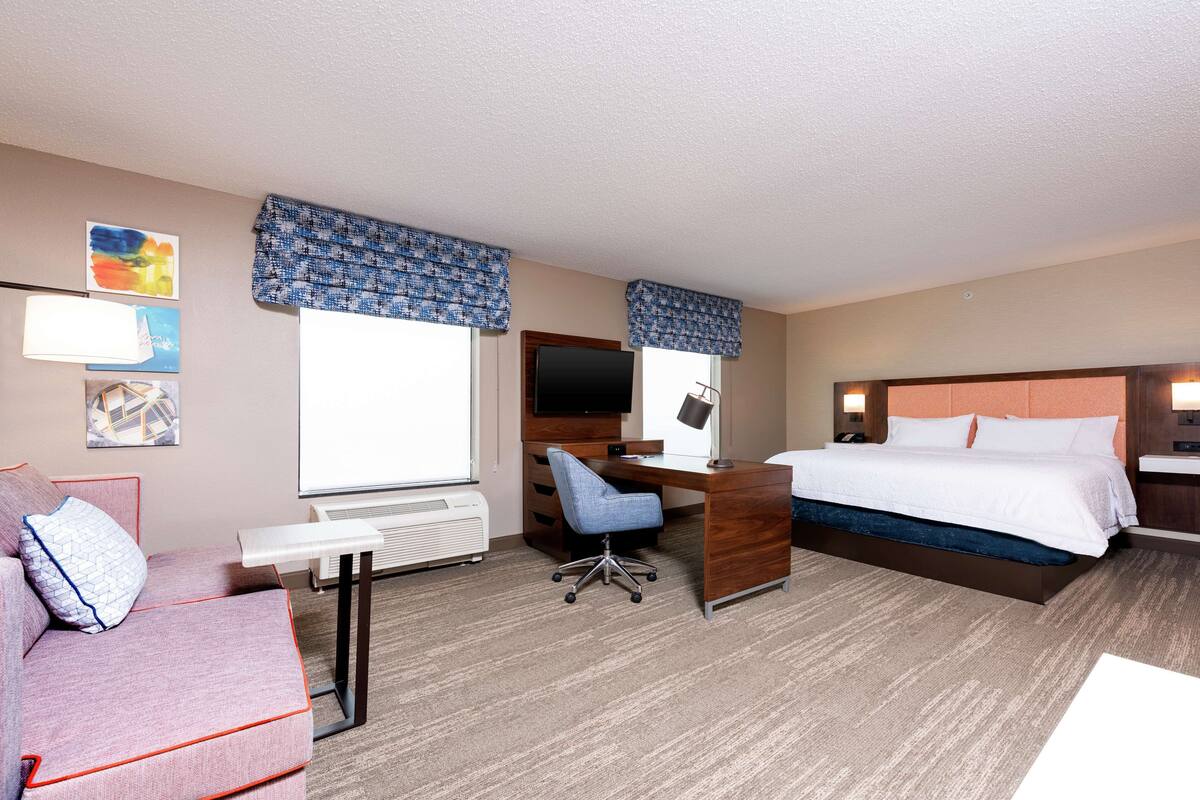 A hotel room with a bed, desk, chair, and a small couch.