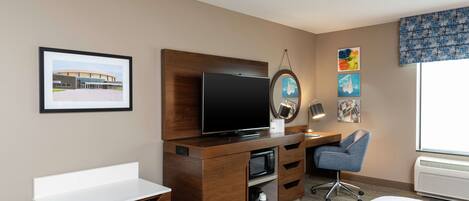 A hotel room with a bed, a desk, a television, a microwave, a chair, and artwork on the walls.