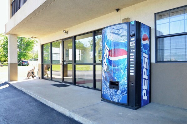 A Pepsi vending machine outside a building with large glass doors and a concrete sidewalk.