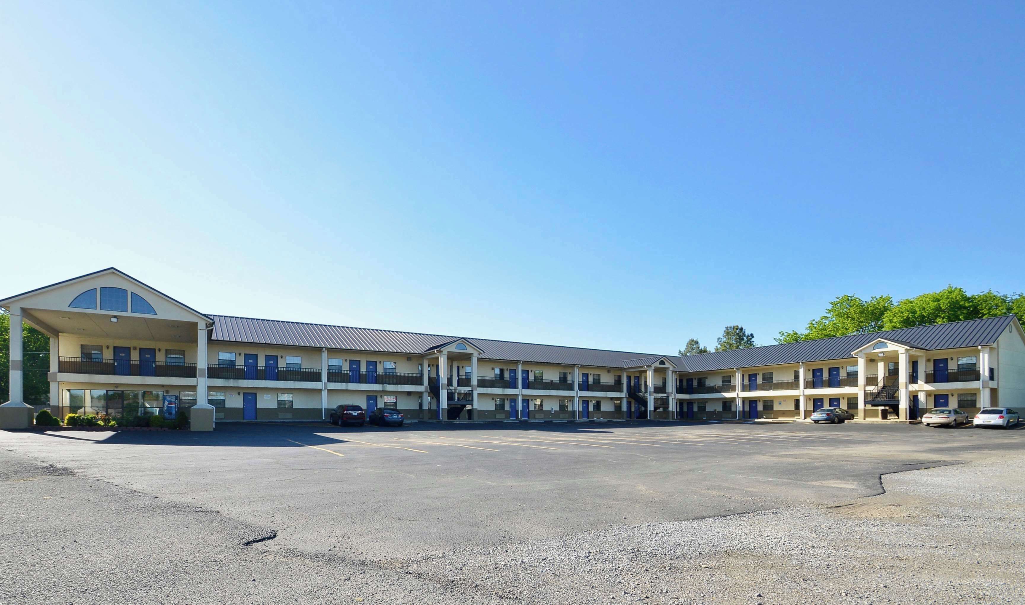 Un motel de varios pisos, con estacionamiento y cielo despejado.