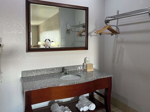 A bathroom with a granite countertop sink, a mirror, a towel rack, and a towel dispenser.