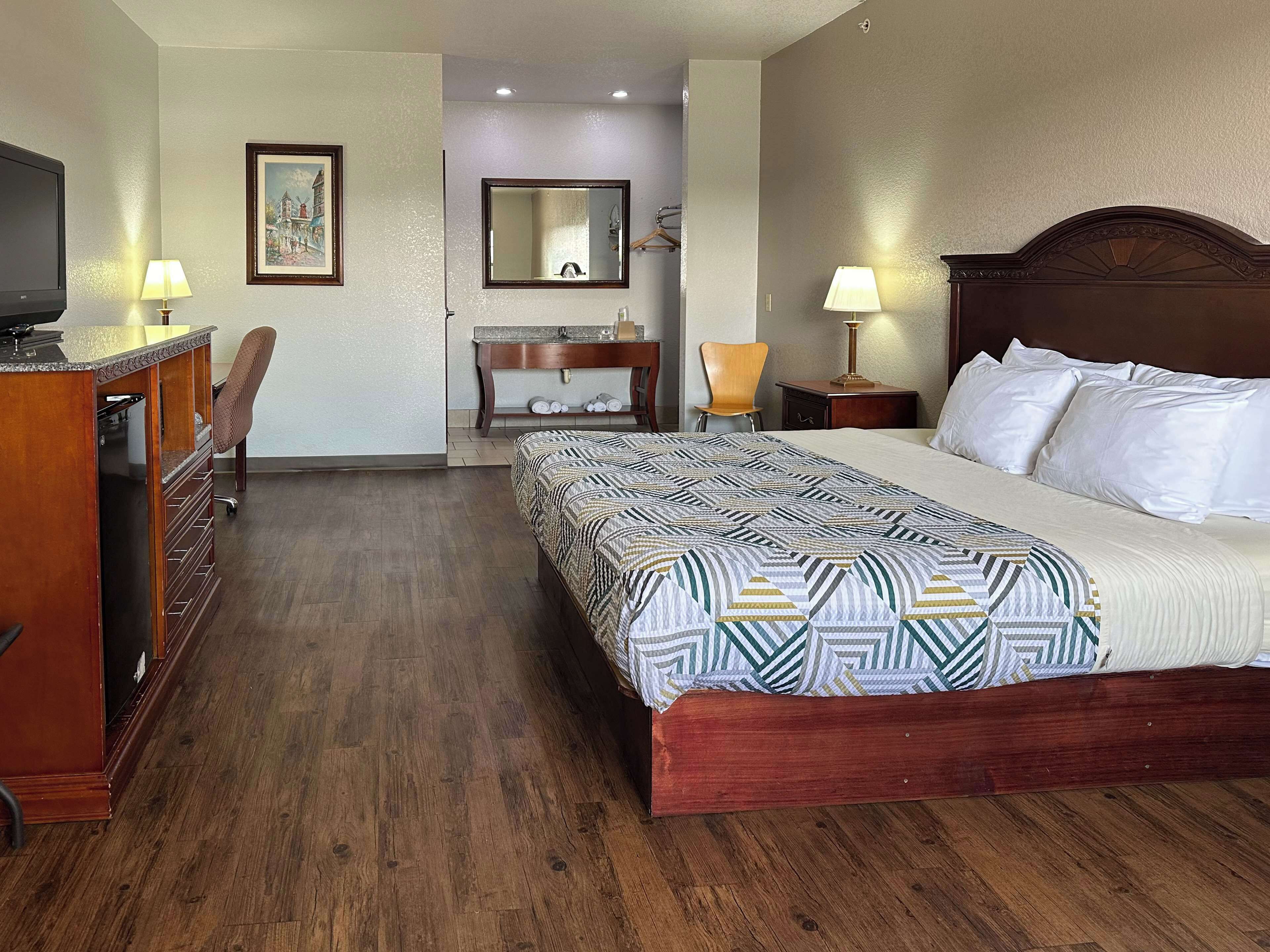 Habitación de hotel con una cama grande, cómoda de madera, escritorio, silla y un espejo.