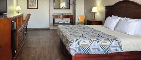 Habitación de hotel con una cama grande, cómoda de madera, escritorio, silla y un espejo.