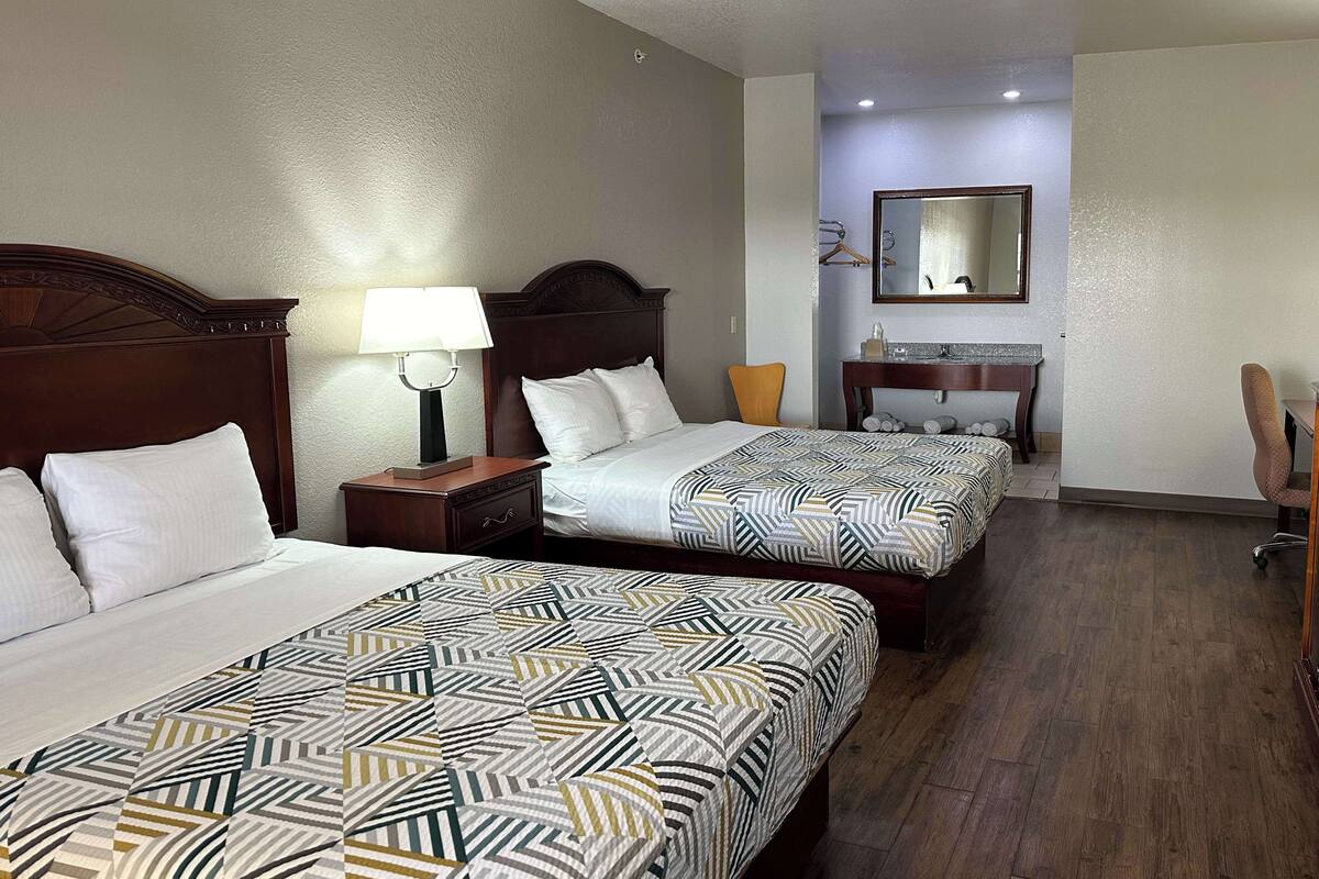 A hotel room with two beds, a desk, a chair, and a mirror.