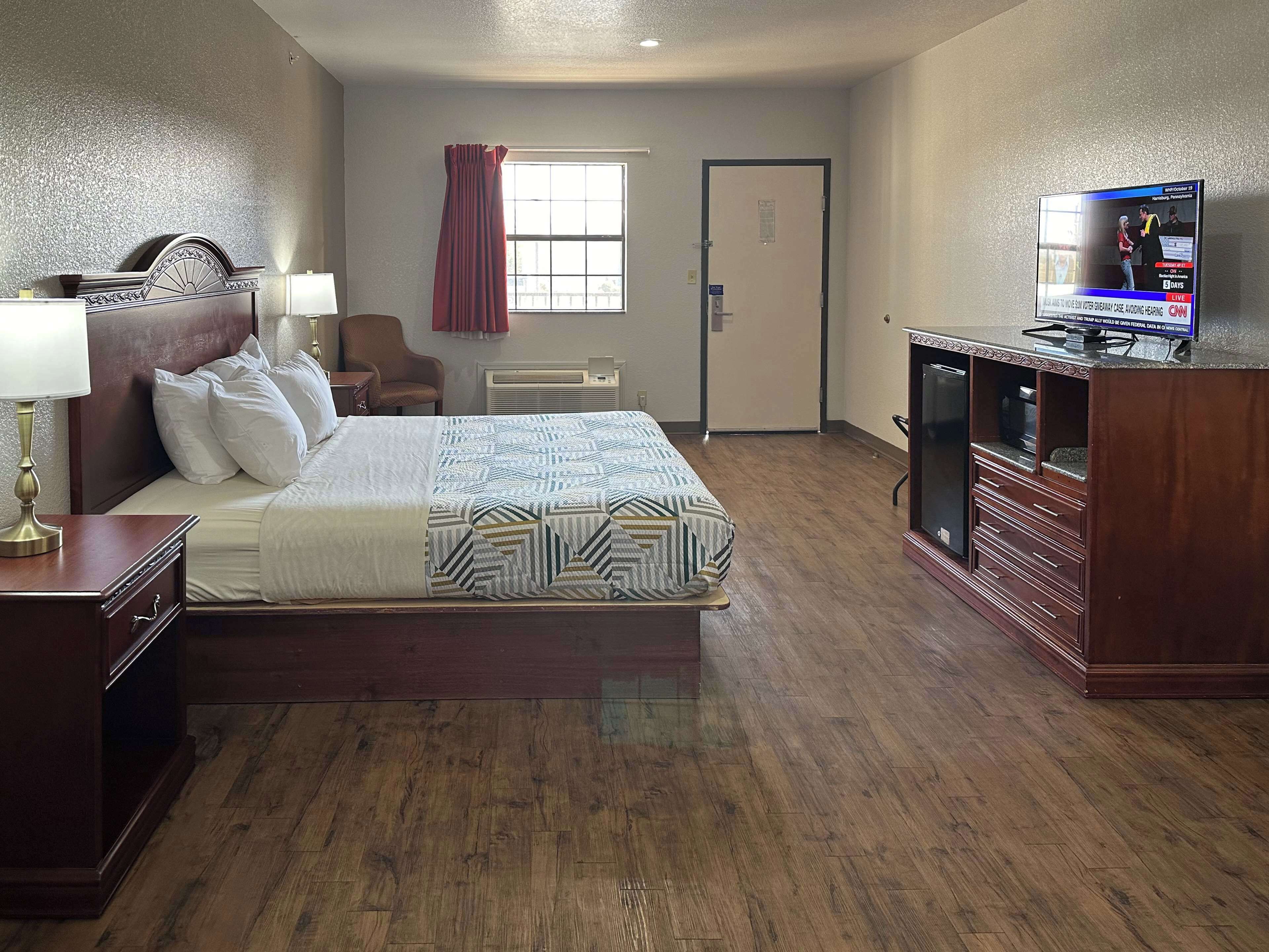 A hotel room with a bed, a desk, a chair, a television, and a door.