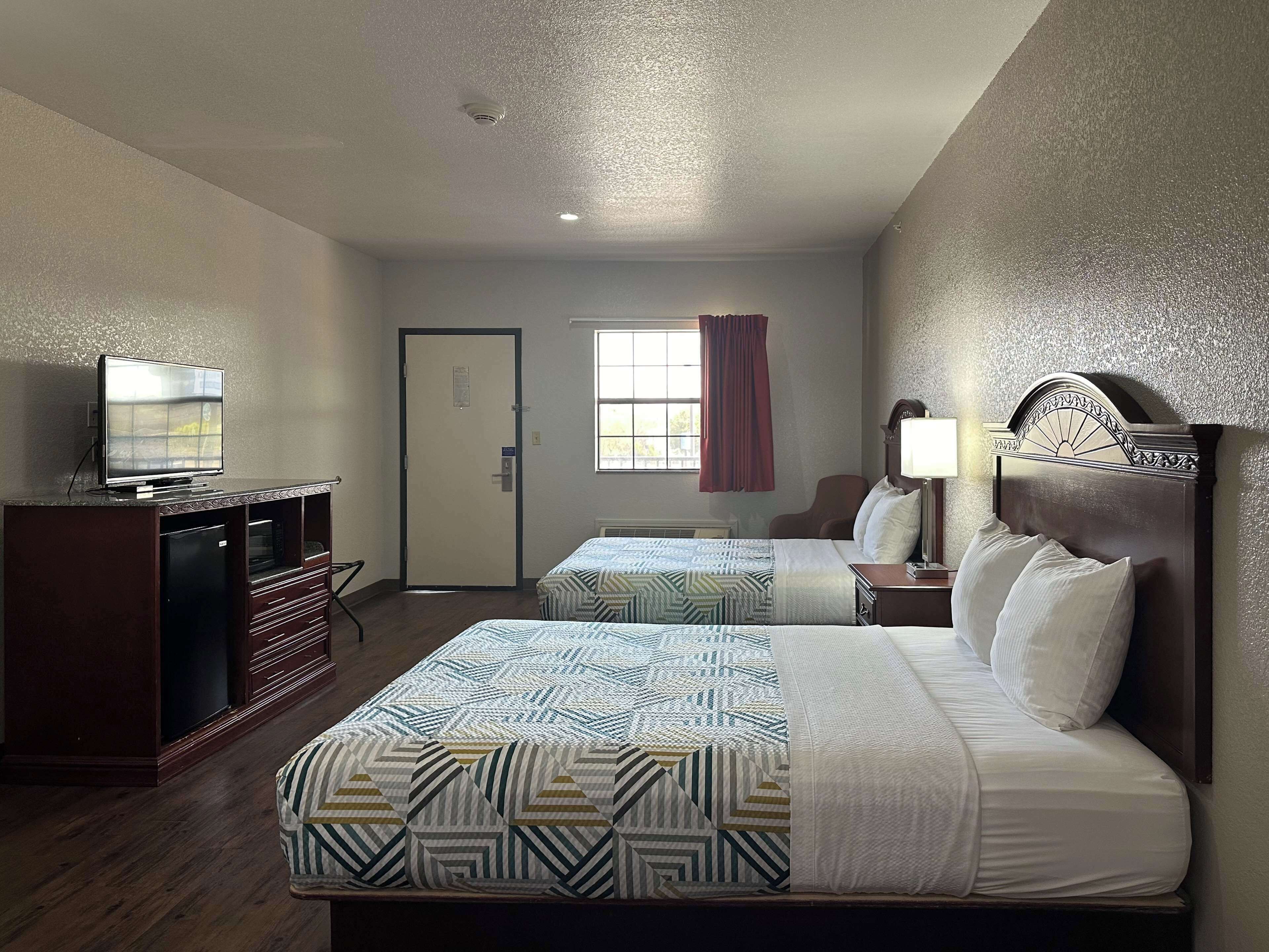 Quarto de hotel com duas camas, televisão, secretária e janela com cortinas.