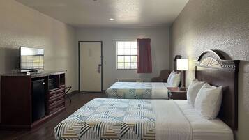 Quarto de hotel com duas camas, televisão, secretária e janela com cortinas.