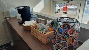 A counter with coffee and tea options, a basket, and a window view of a parking area. - Motel Reedsburg (Reedsburg)