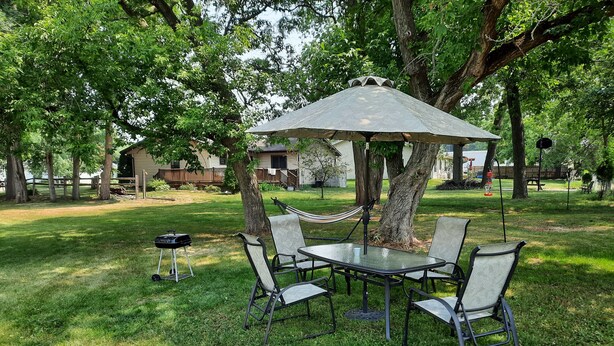 A picnic table with four chairs and a large umbrella, surrounded by trees in a grassy area. - Motel Reedsburg (Reedsburg)