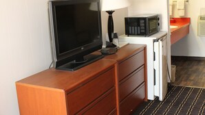 Ein Hotelzimmer mit einem Holzkasten, einem Fernseher, einer Mikrowelle und einer kleinen Mülltonne.