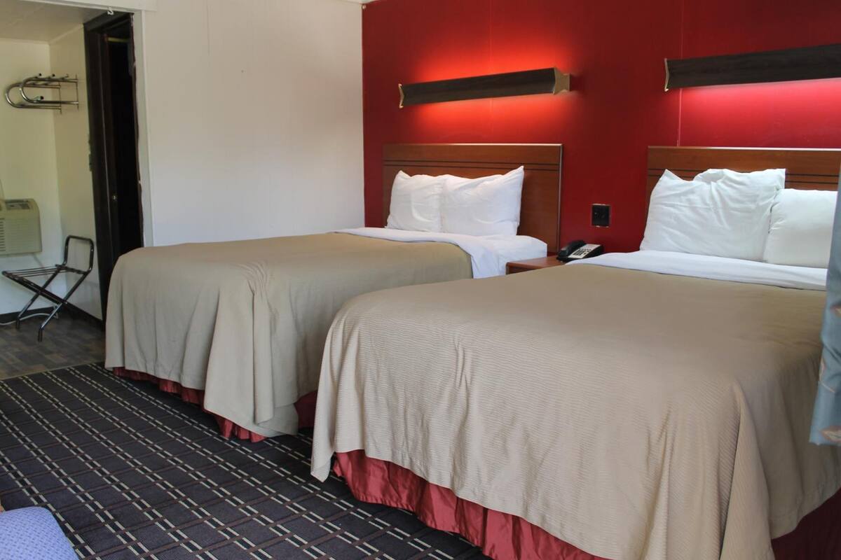 A hotel room with two beds, a red accent wall, a striped rug, and a visible telephone.