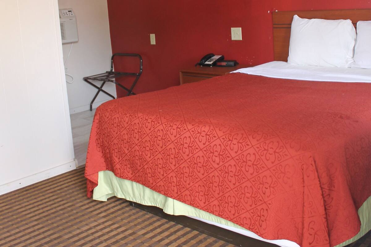 A hotel room with a large bed, a chair, a nightstand, and a wall-mounted heater.