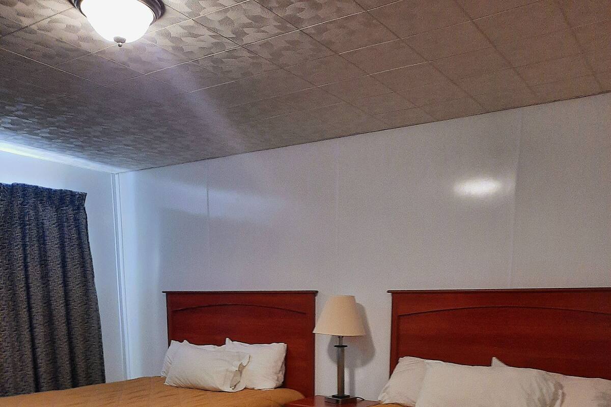 A hotel room with two beds, wooden headboards, a nightstand with a lamp, and a window with curtains.