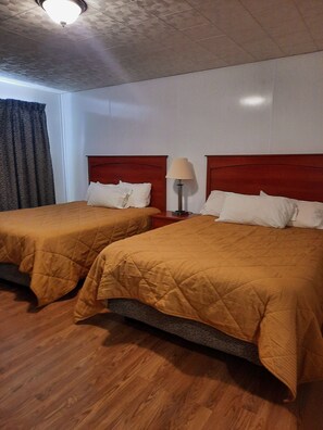 A hotel room with two beds, wooden headboards, a nightstand with a lamp, and a window with curtains.