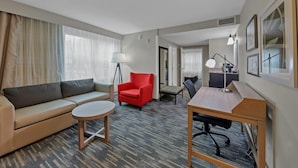 A hotel room with a sofa, armchair, desk, lamp, and framed pictures on the wall. - Country Inn & Suites by Radisson, Braselton, GA (Hoschton)