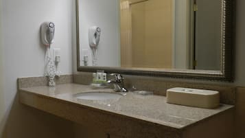 A bathroom with a granite countertop, a sink, a mirror, and two hair dryers mounted on the wall.