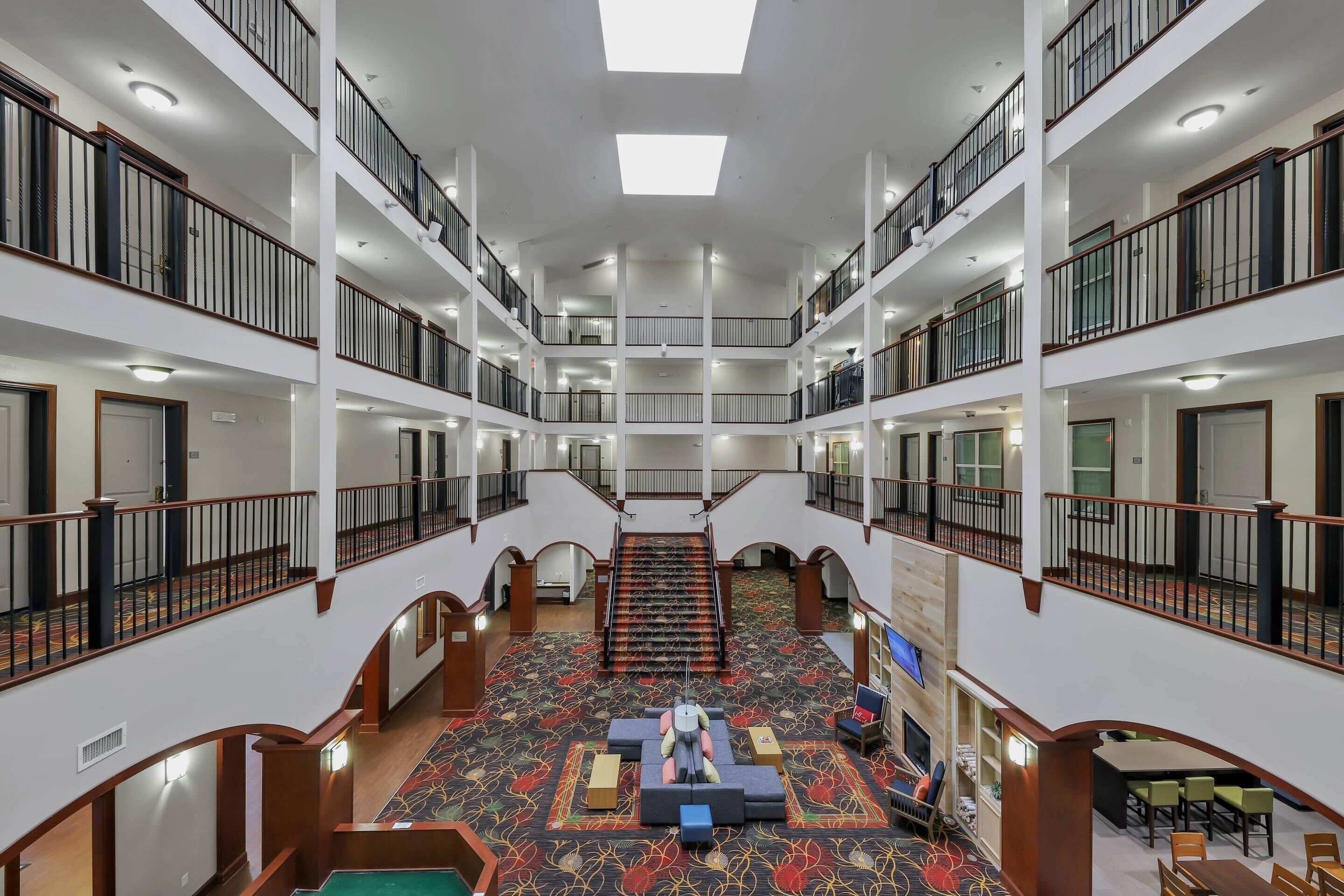 A multi-level hotel lobby with a central staircase, multiple balconies, and a carpeted floor.
