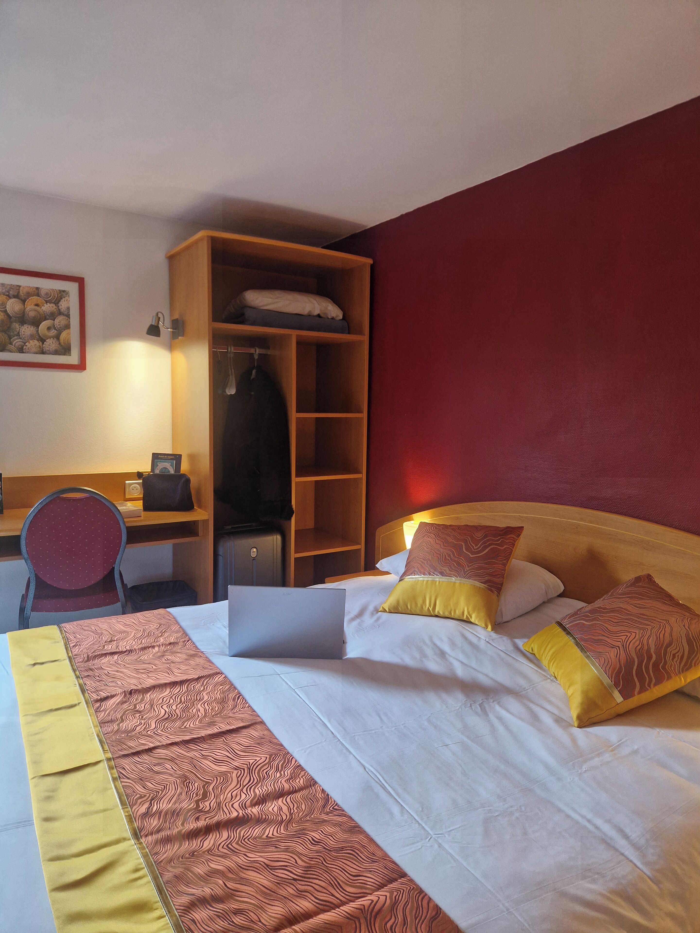 A hotel room with a bed, a desk, a chair, and a wardrobe.