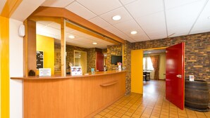 Un espace d’accueil avec un comptoir en bois, un miroir, un téléviseur et une porte rouge.