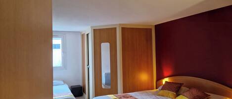 Habitación de hotel con una cama grande, una cama más pequeña, un armario y una ventana.