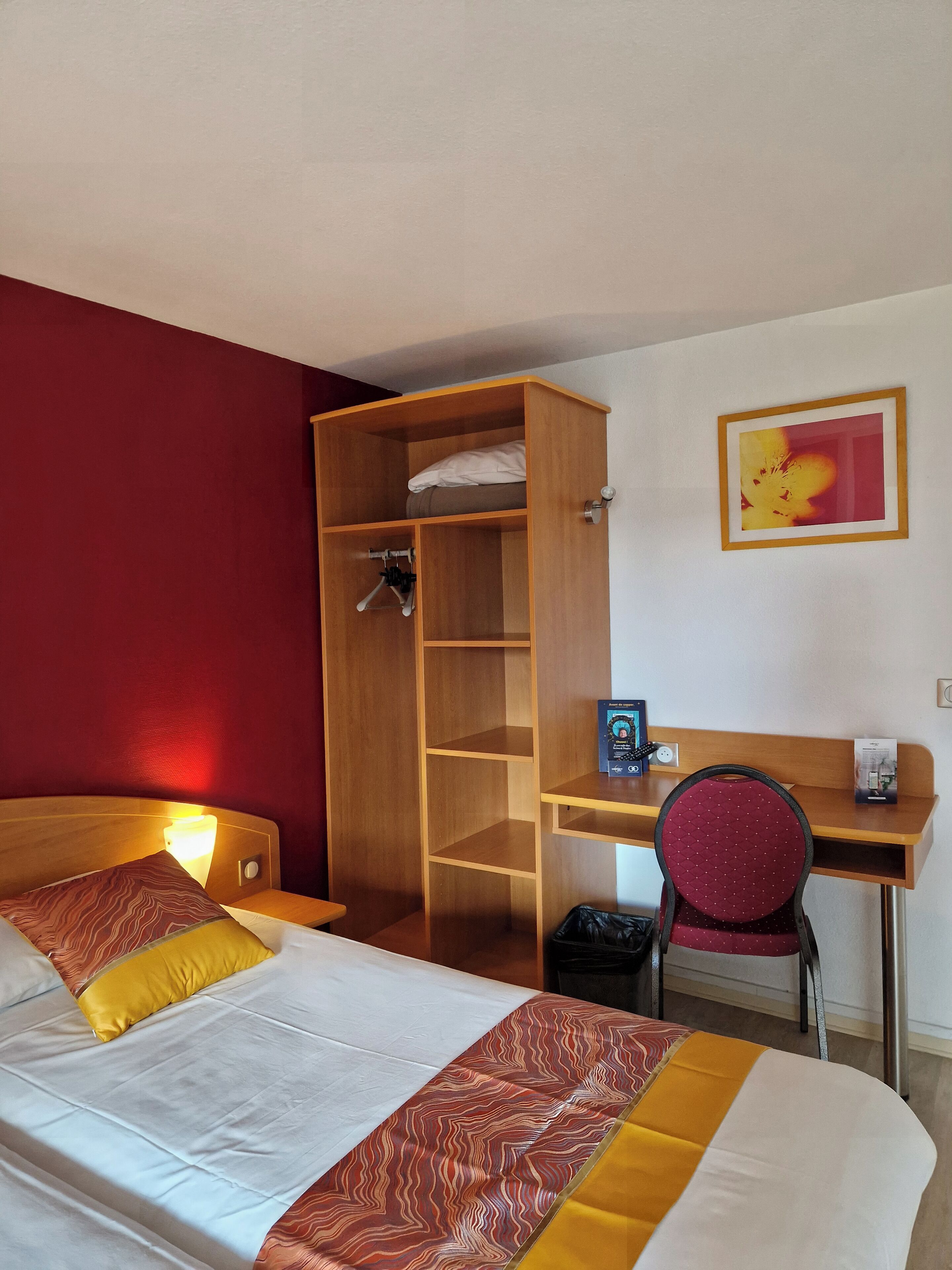 Una camera d'albergo con un letto, un armadio in legno, una scrivania con una sedia e un quadro appeso al muro.