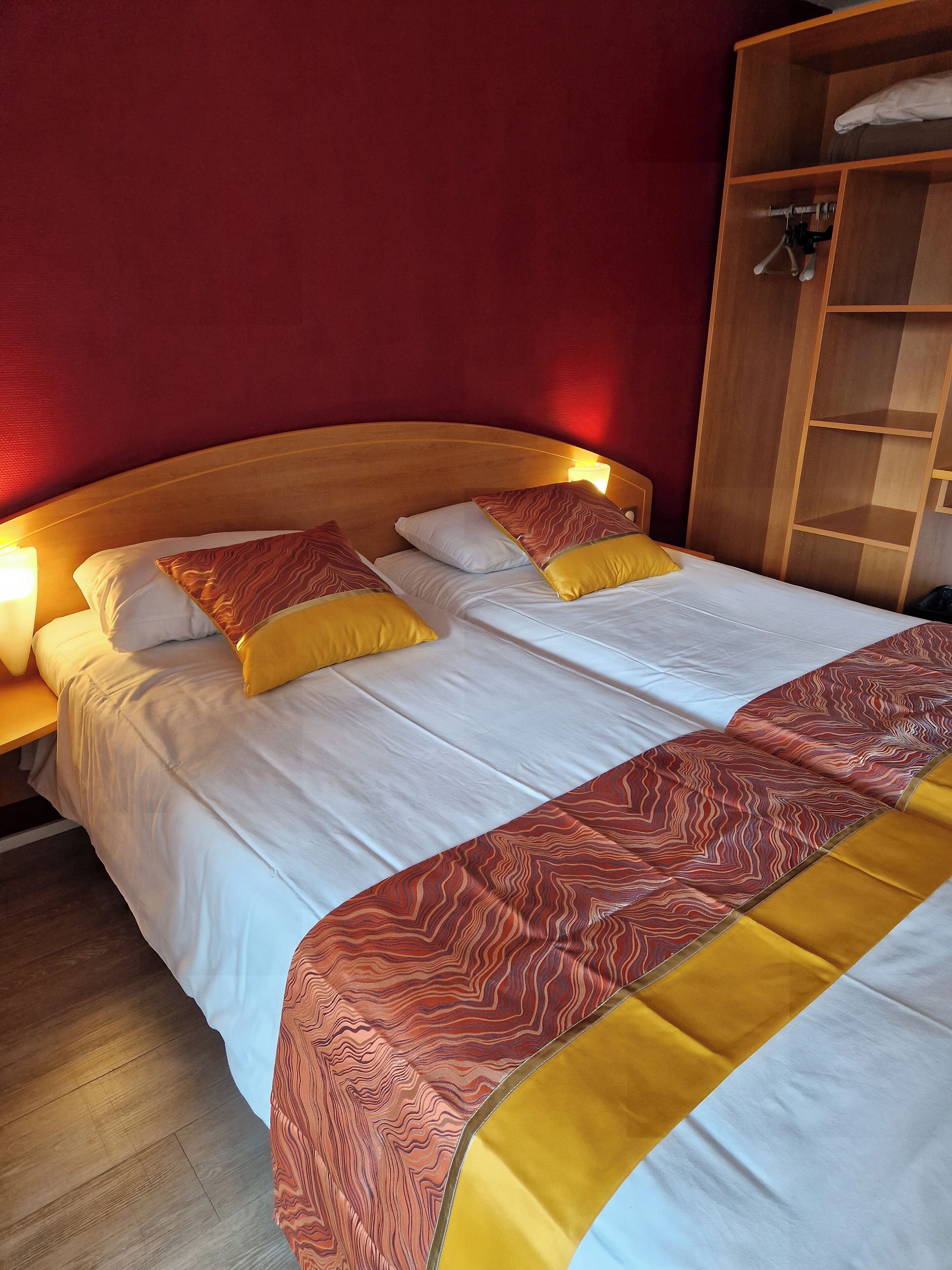 A double bed with white bedding and two yellow pillows, a wooden headboard, and a wooden wardrobe with a mirror.