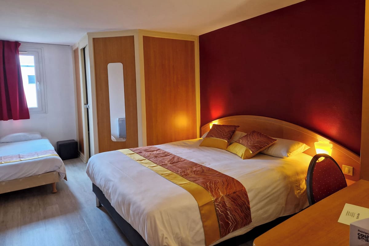 Habitación de hotel con dos camas, cabecero de madera, un espejo y una pared de acento roja.