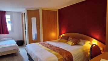 A hotel room with two beds, a wooden headboard, a mirror, and a red accent wall.