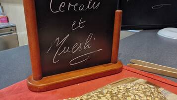 A loaf of bread with oats on top, placed on a cutting board next to a blackboard menu.