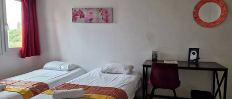 A hotel room with two single beds, a desk with a chair, a small trash bin, and a wall-mounted mirror.